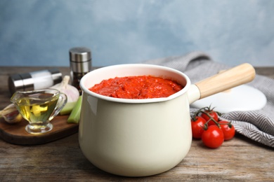 Photo of Pan of tomato sauce on wooden table against blue background