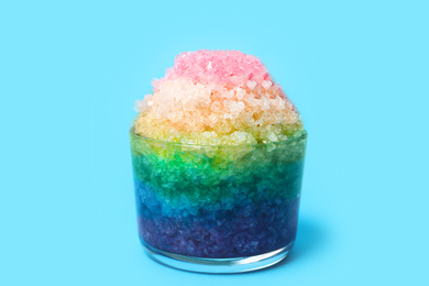 Photo of Rainbow shaving ice in glass dessert bowl on light blue background, closeup