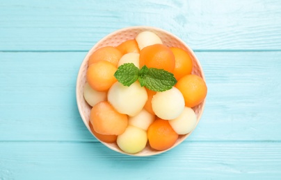 Photo of Melon balls and mint in bowl on light blue table, top view