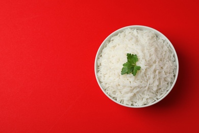 Bowl of cooked rice with parsley on color background, top view. Space for text