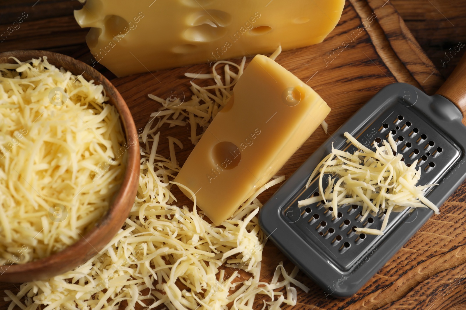 Photo of Grated, cut cheese and grater on wooden board, above view