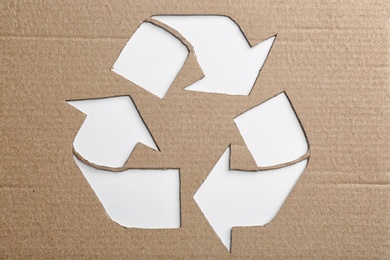 Photo of Sheet of cardboard with cutout recycling symbol on white background, top view