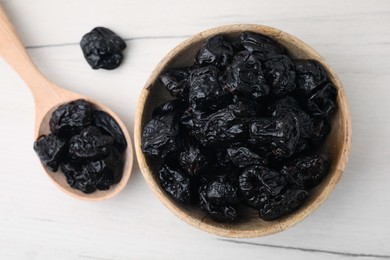Bowl and spoon with sweet dried prunes on white wooden table, flat lay