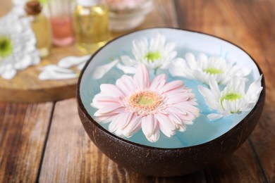 Photo of Bowl with water and beautiful flowers on wooden table, closeup. Spa composition