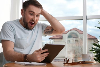 Photo of Emotional man participating in online auction using tablet at home