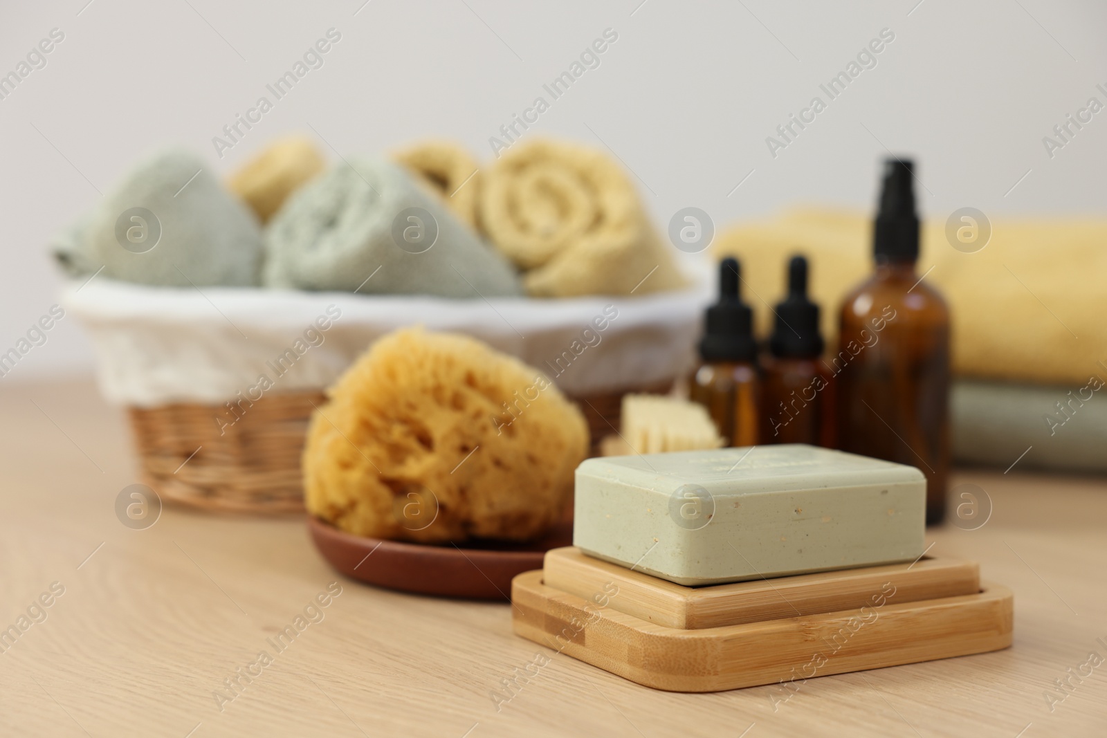 Photo of Soap bar, sponge and bottles of essential oils on light wooden table. Spa therapy