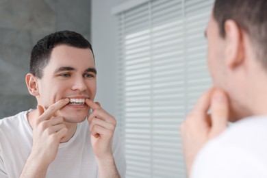 Photo of Young man applying whitening strip on his teeth indoors