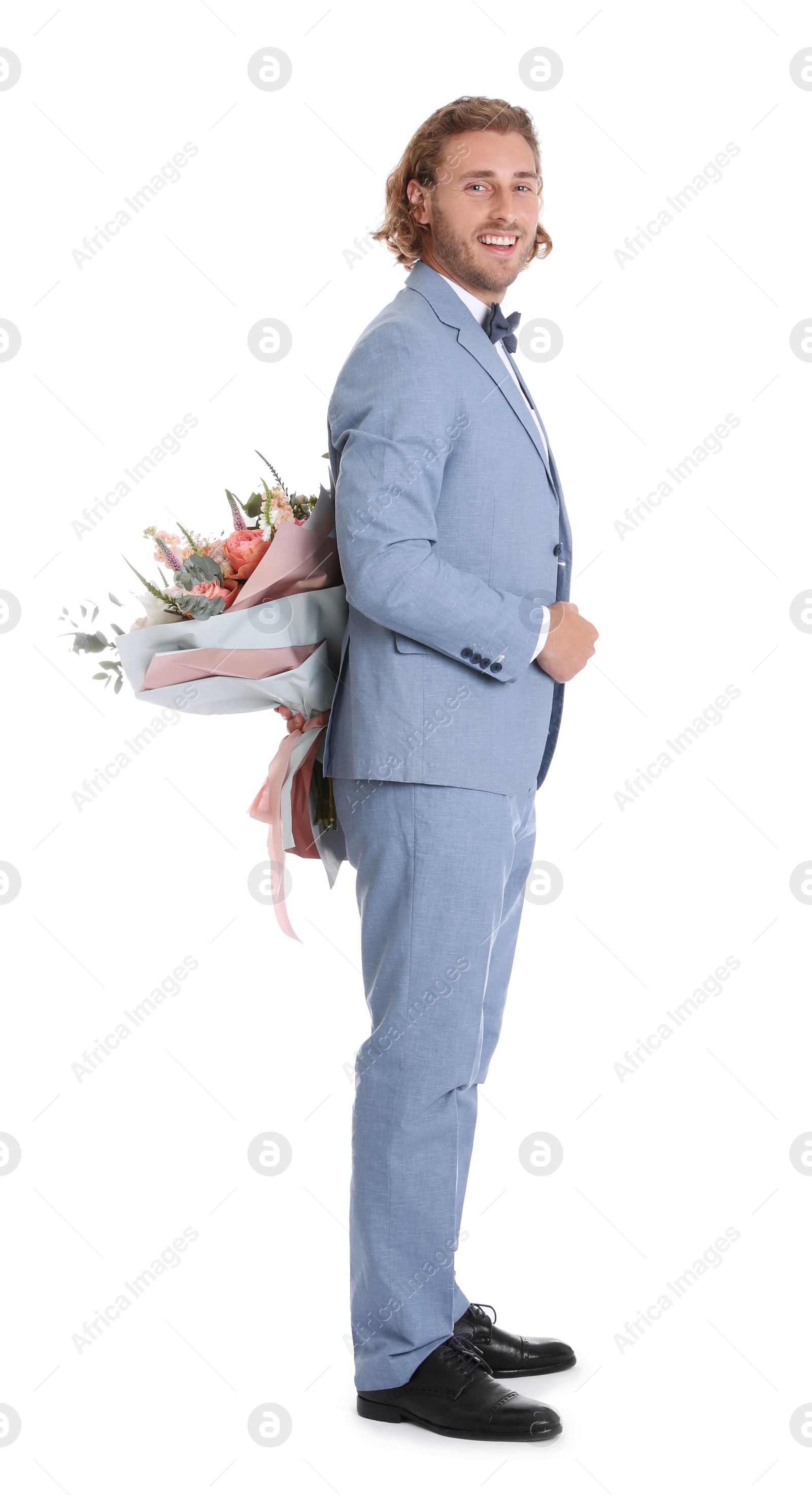 Photo of Young handsome man in stylish suit hiding beautiful flower bouquet behind his back on white background