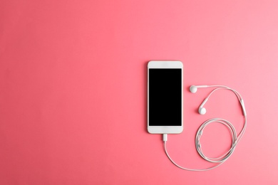 Photo of Modern phone with earphones on pink background, top view. Space for text