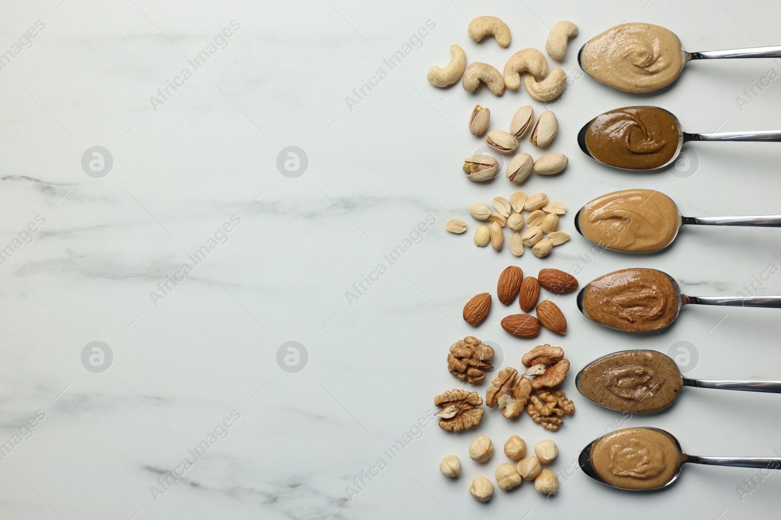 Photo of Tasty nut butters in spoons and raw nuts on white marble table, flat lay. Space for text