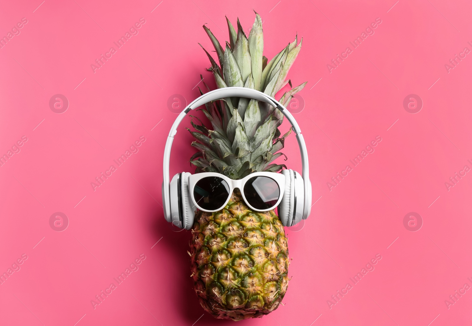 Photo of Pineapple with sunglasses and headphones on pink background, top view. Creative concept