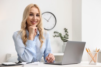 Photo of Happy secretary at table with laptop and stationery in office