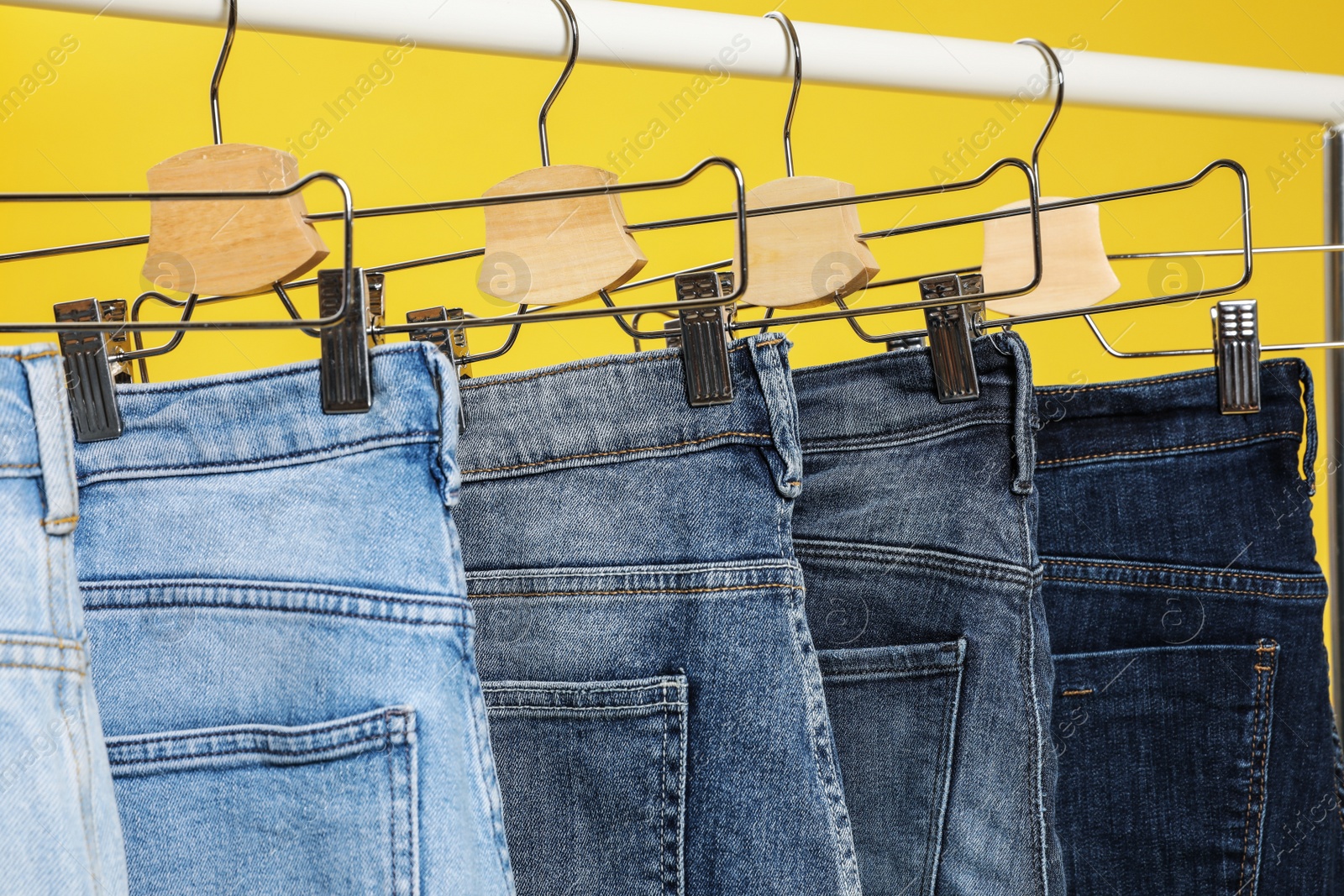 Photo of Rack with different jeans on yellow background, closeup