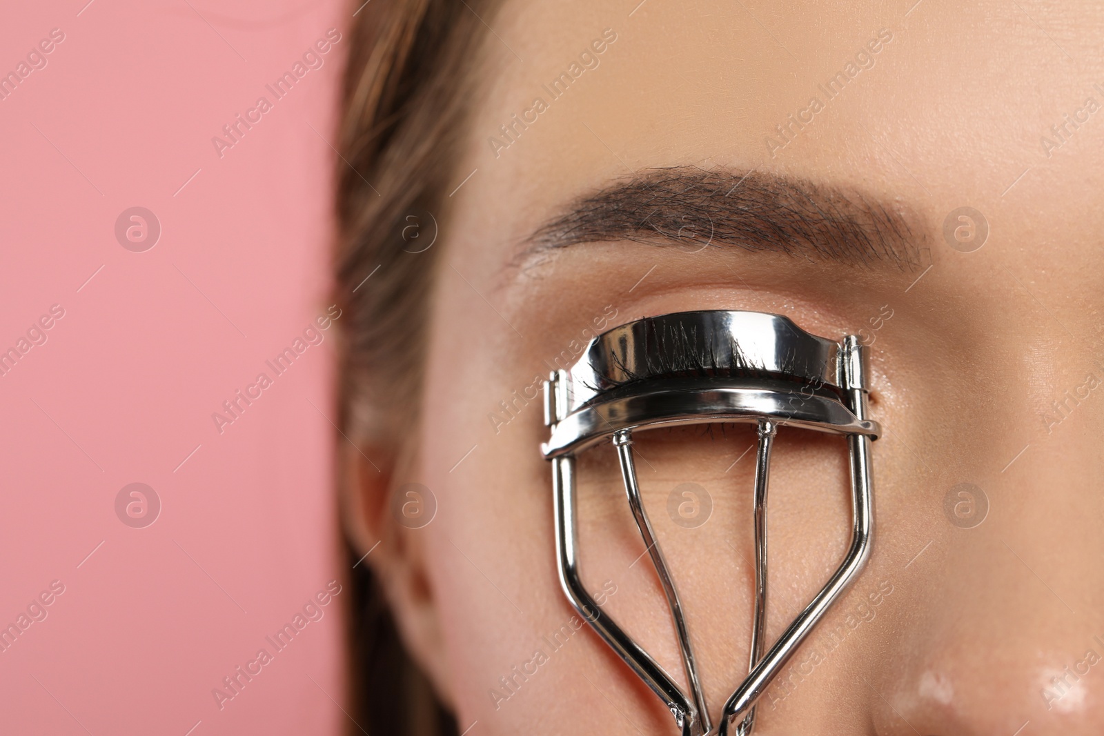 Photo of Woman using eyelash curler on pink background, closeup. Space for text