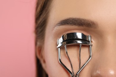 Photo of Woman using eyelash curler on pink background, closeup. Space for text