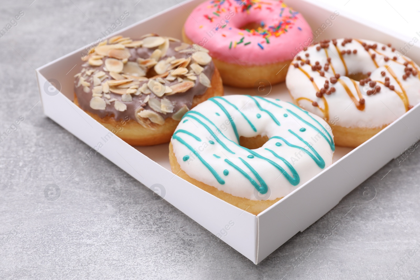 Photo of Box with different tasty glazed donuts on light grey table, closeup