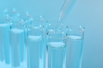 Photo of Laboratory analysis. Dripping reagent into test tube on light blue background, closeup