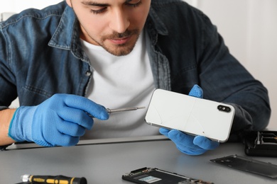 Photo of Technician repairing broken smartphone at table, closeup