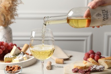 Photo of Woman pouring white wine from bottle into glass at table with snacks, closeup