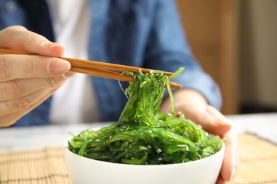 Photo of Woman eating Japanese seaweed salad at table, closeup