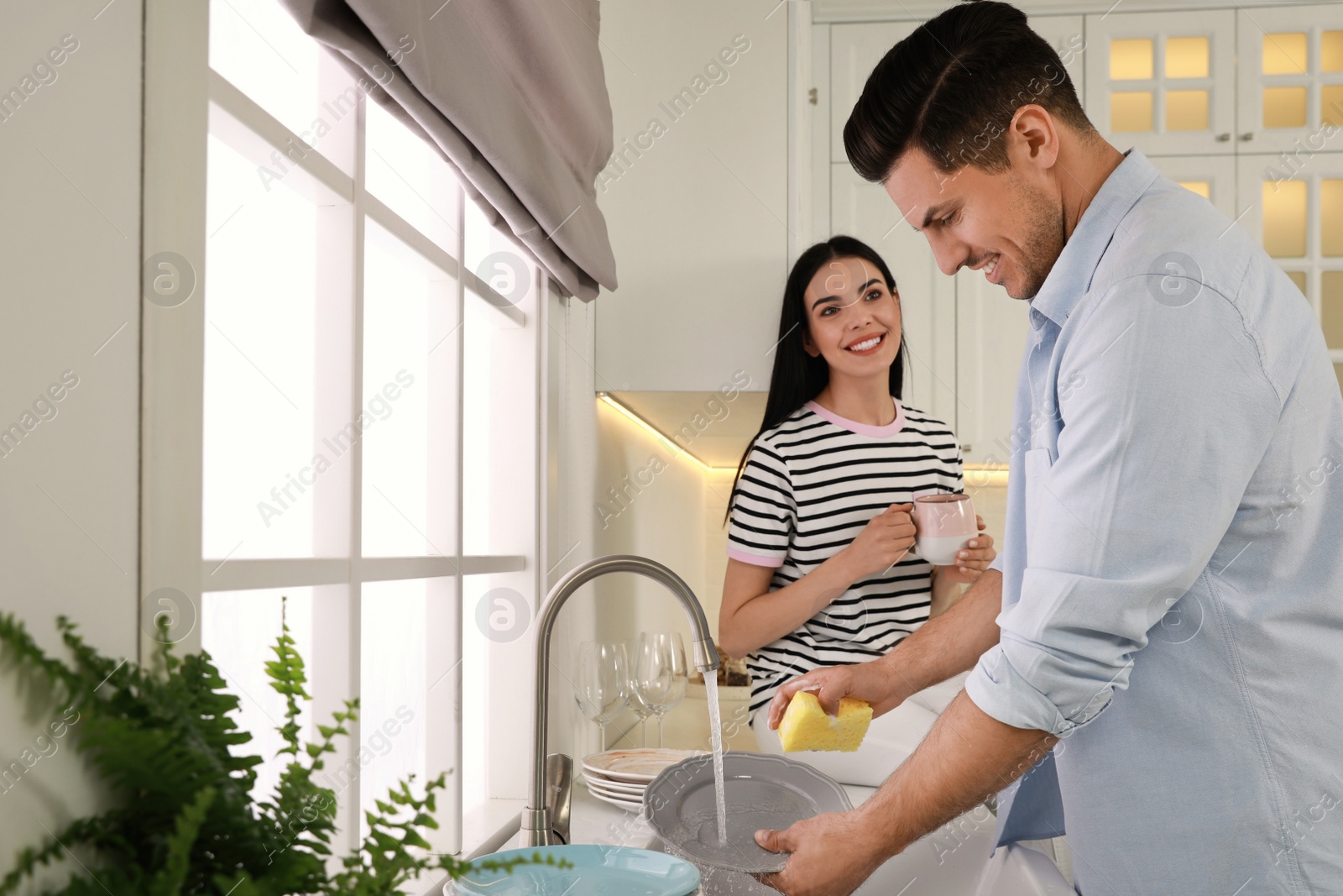 Photo of Man washing plate and talking with woman in kitchen