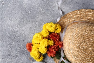 Flat lay composition with bright chrysanthemum flowers and wicker hat on grey textured table. Space for text