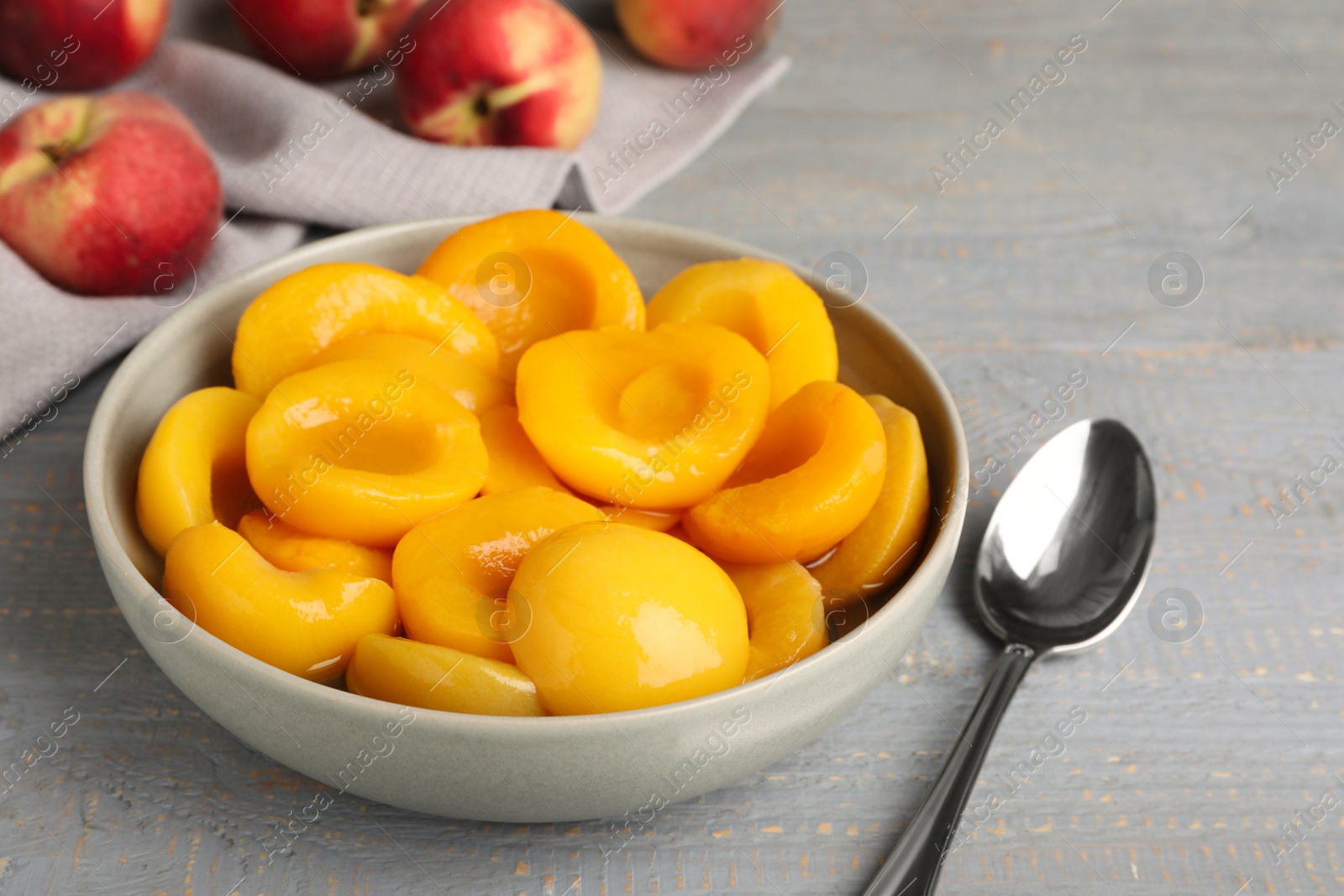 Photo of Canned peach halves and spoon on grey wooden table