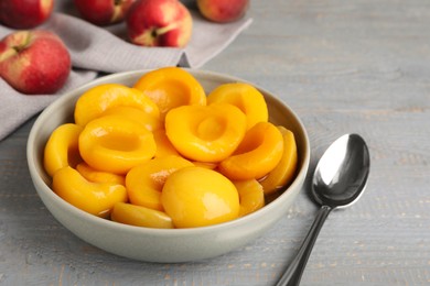 Canned peach halves and spoon on grey wooden table