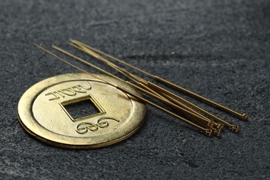 Acupuncture needles and Chinese coin on grey textured table, closeup