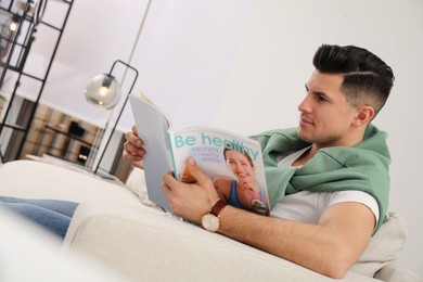 Photo of Man reading magazine on sofa in living room
