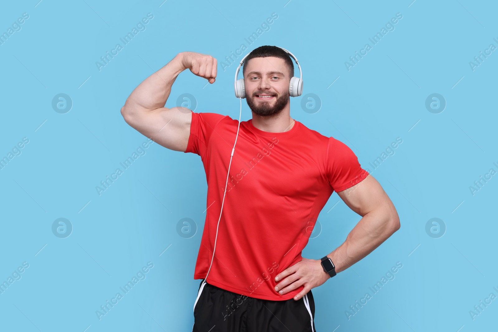 Photo of Handsome man with headphones showing muscles on light blue background