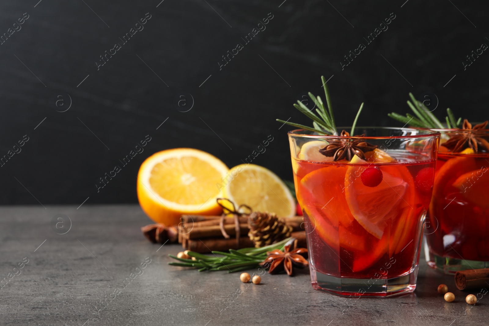 Photo of Delicious punch drink with cranberries, orange and spices on grey table. Space for text