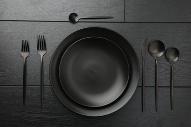 Photo of Stylish setting with cutlery and plates on black wooden table, flat lay