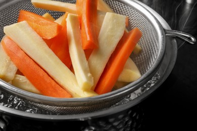 Sieve with cut parsnips and carrots over pot of boiling water, closeup
