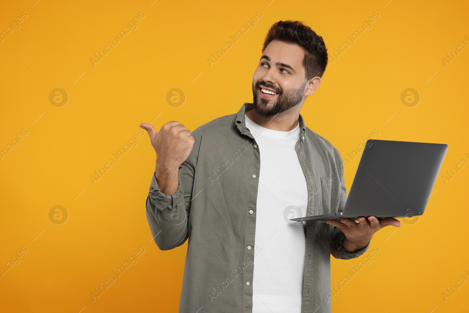 Photo of Special promotion. Smiling man with laptop pointing at something on orange background. Space for text