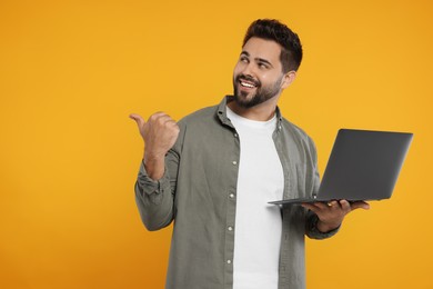 Photo of Special promotion. Smiling man with laptop pointing at something on orange background. Space for text