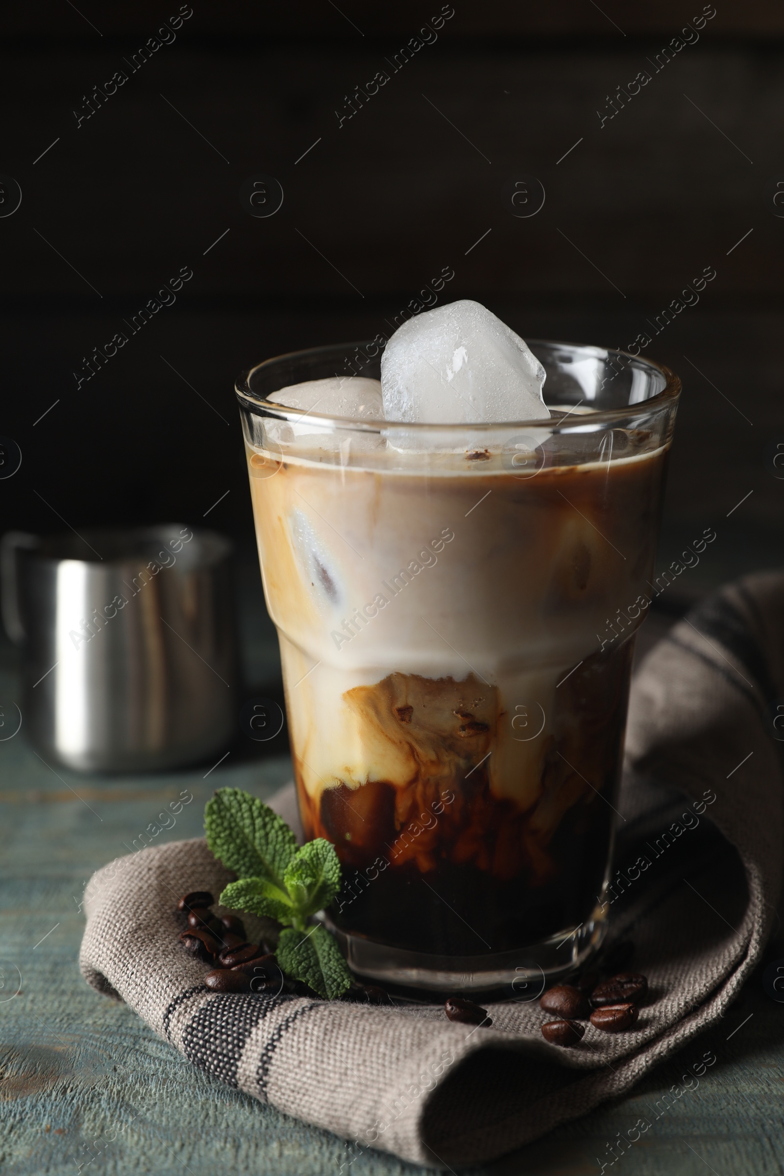 Photo of Glass of delicious iced coffee with milk, beans and mint on light blue wooden table