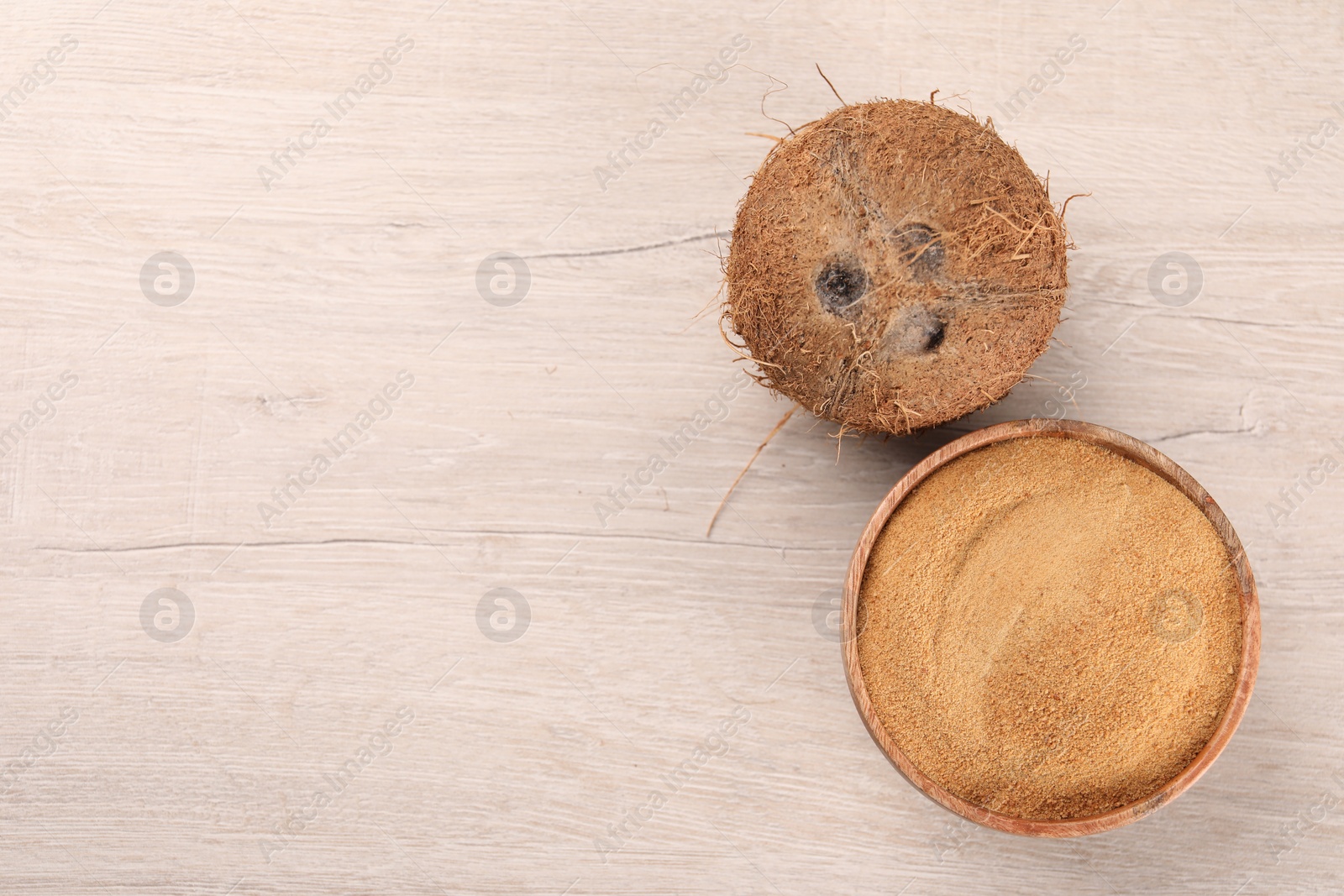 Photo of Coconut sugar in bowl and fruit on light wooden table, top view. Space for text