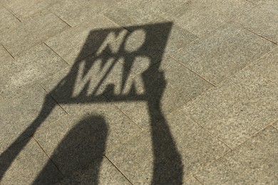 Photo of Shadow of woman holding poster with words No War outdoors