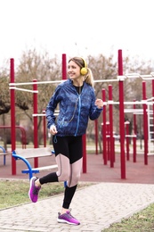 Young woman with headphones listening to music and exercising on sports ground