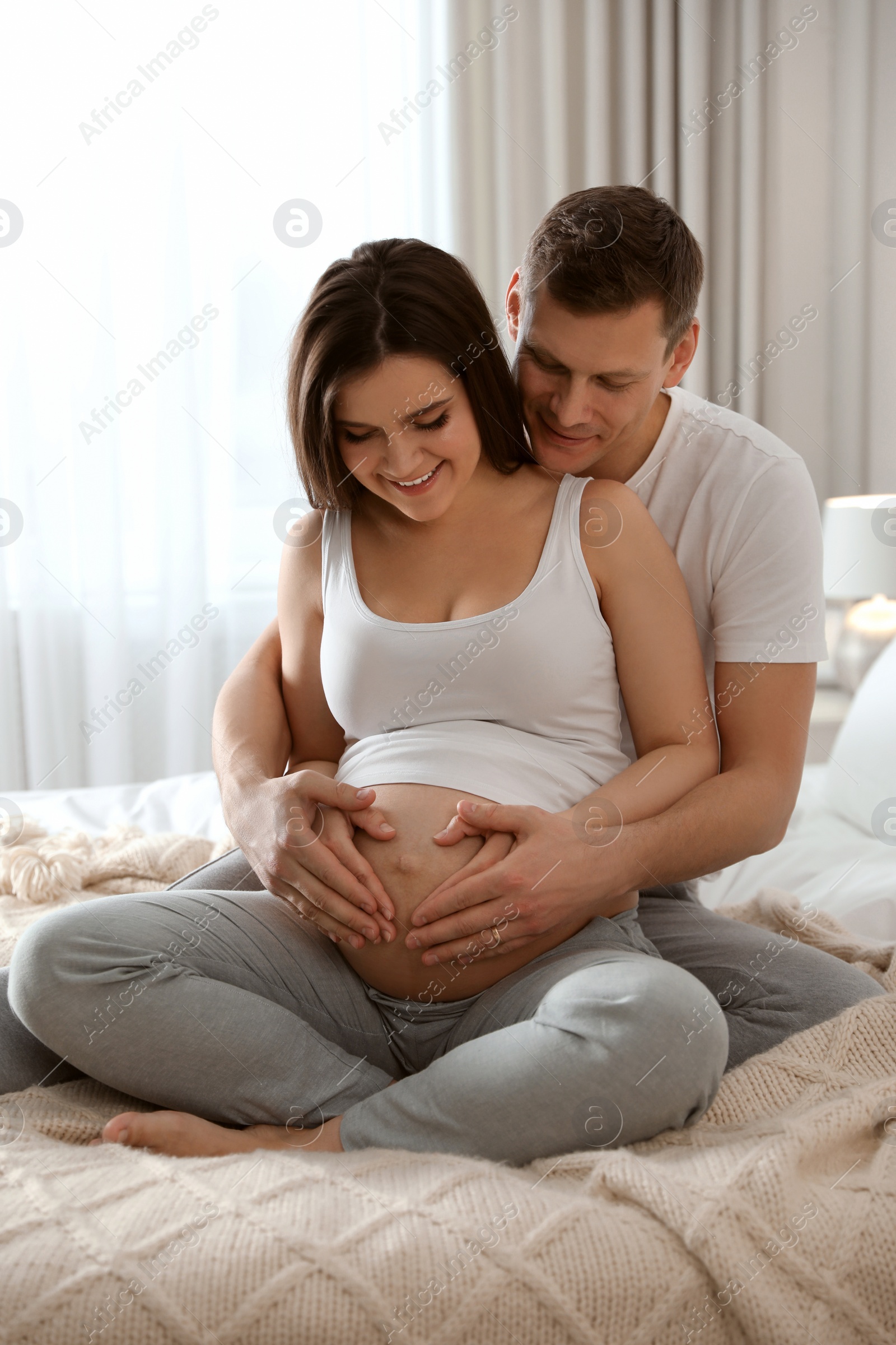 Photo of Young pregnant woman with her husband in bedroom