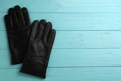 Stylish black leather gloves on turquoise wooden background, flat lay. Space for text