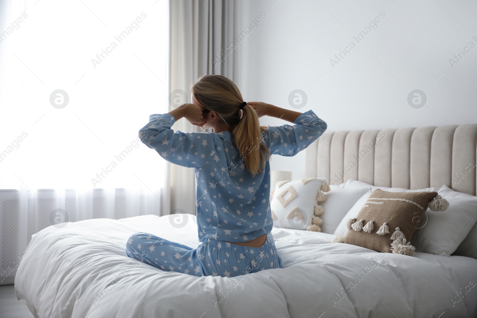 Photo of Young woman stretching on bed at home, back view. Morning fitness