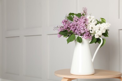 Photo of Beautiful lilac flowers in vase on wooden table near white wall. Space for text