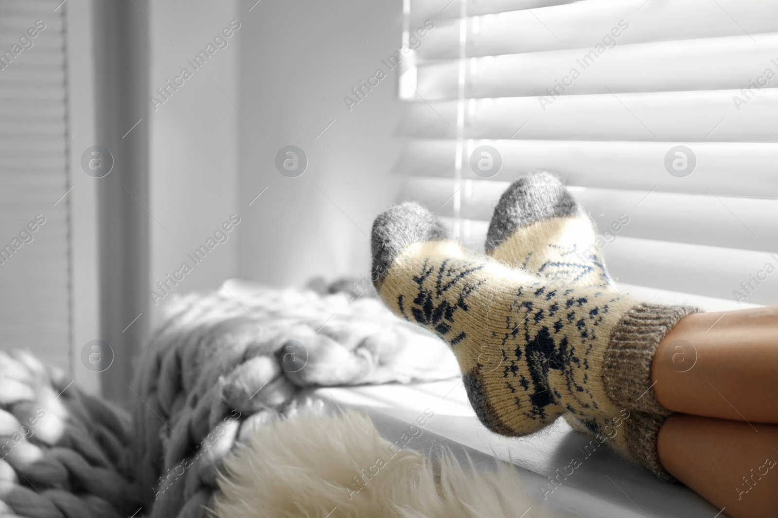 Photo of Woman wearing knitted socks on window sill indoors, closeup. Warm clothes