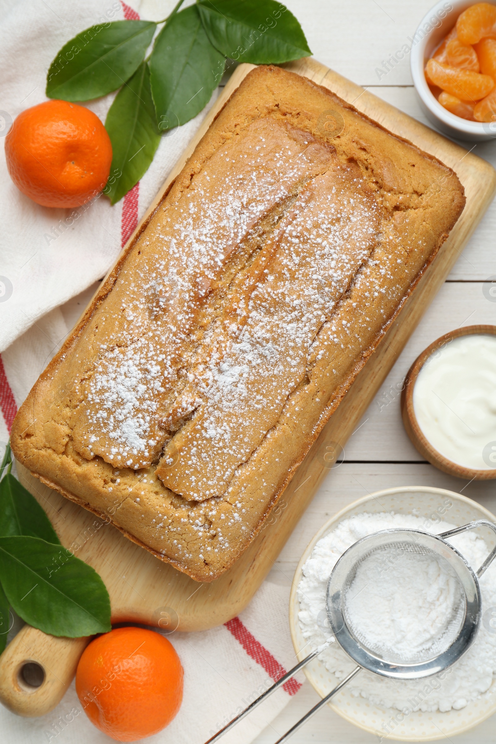 Photo of Delicious homemade yogurt cake with powdered sugar and tangerines on white wooden table, flat lay