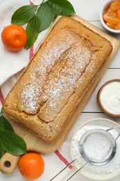 Delicious homemade yogurt cake with powdered sugar and tangerines on white wooden table, flat lay