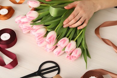 Photo of Woman making bouquet of beautiful fresh tulips at white wooden table, closeup