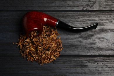 Photo of Smoking pipe and dry tobacco on black wooden table, flat lay