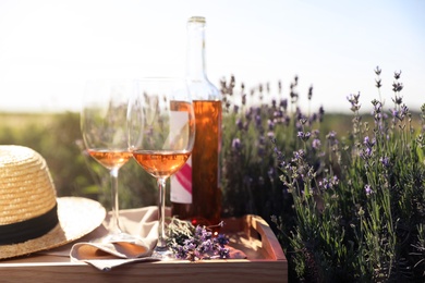 Photo of Bottle and glasses of wine on wooden table in lavender field. Space for text